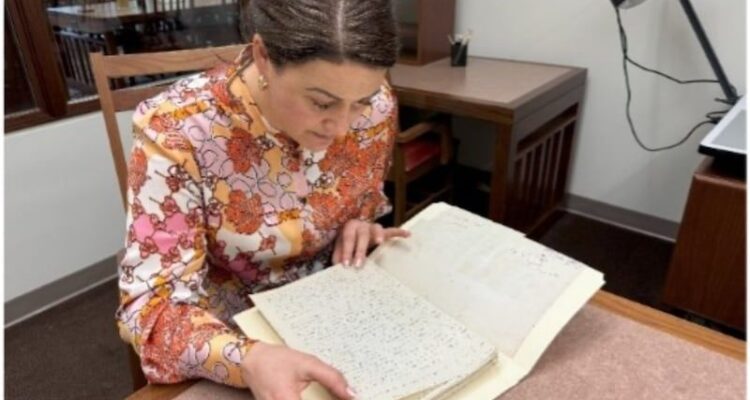 Frau betrachtet ein aufgeschlagenes handschriftliches Manuskript am Schreibtisch